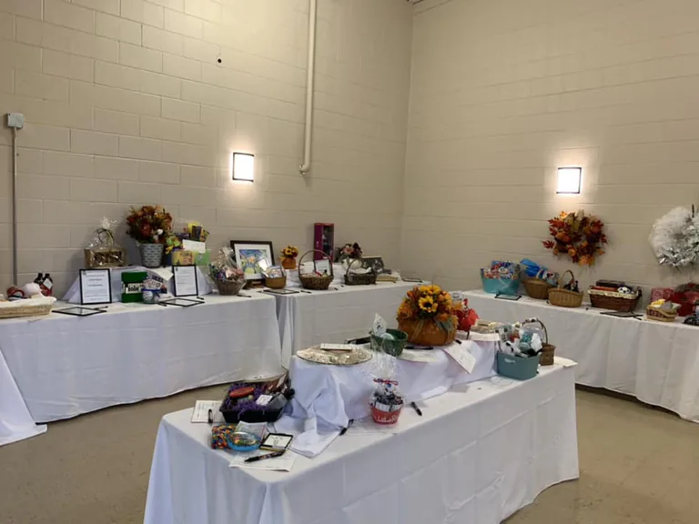 Silent auction tables with gift baskets and bid sheets set up in a school hall